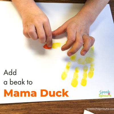 A yellow mama duck is made from a stamped handprint and a child is adding an orange paper beak.